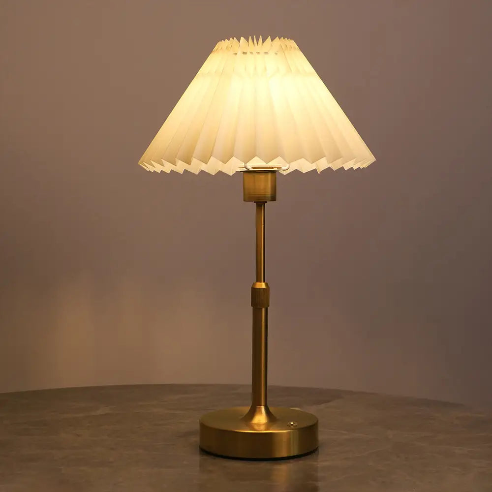 Eine warmtonige Messing-Touch-Tischlampe mit einem plissierten off-weißen Papierschirm, von vorn dargestellt.