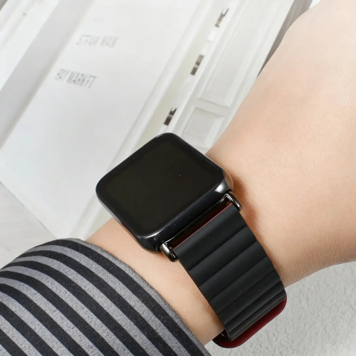 Schwarzes Silikon-Magnetarmband für die Smartwatch mit dezentem rotem Innenfutter, am Handgelenk getragen, passend zur schwarzen Xiaomi Redmi Smartwatch.