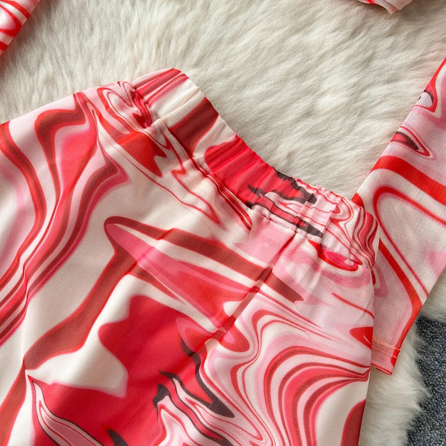 A vibrant red and white marbled patterned two piece mesh skirt set featuring a flowing sheer top with an elastic closure type.