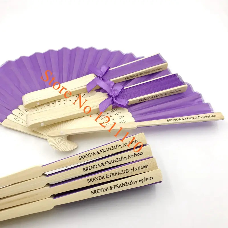 Custom wedding hand fans made of bamboo and silk in purple and beige colors with engraved names and date tied together by a matching purple ribbon.