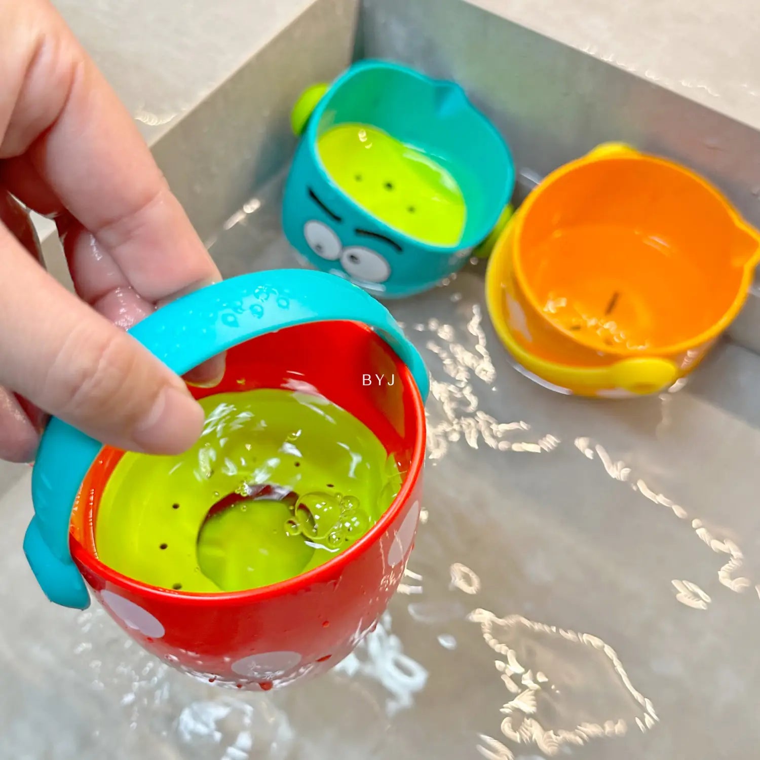 Hellrote und blaue Kunststoff-Badewannen-Eimer für Babys mit Wassersprühfunktion, mit grünem Innenbereich und weißen Punkten auf der Außenseite.