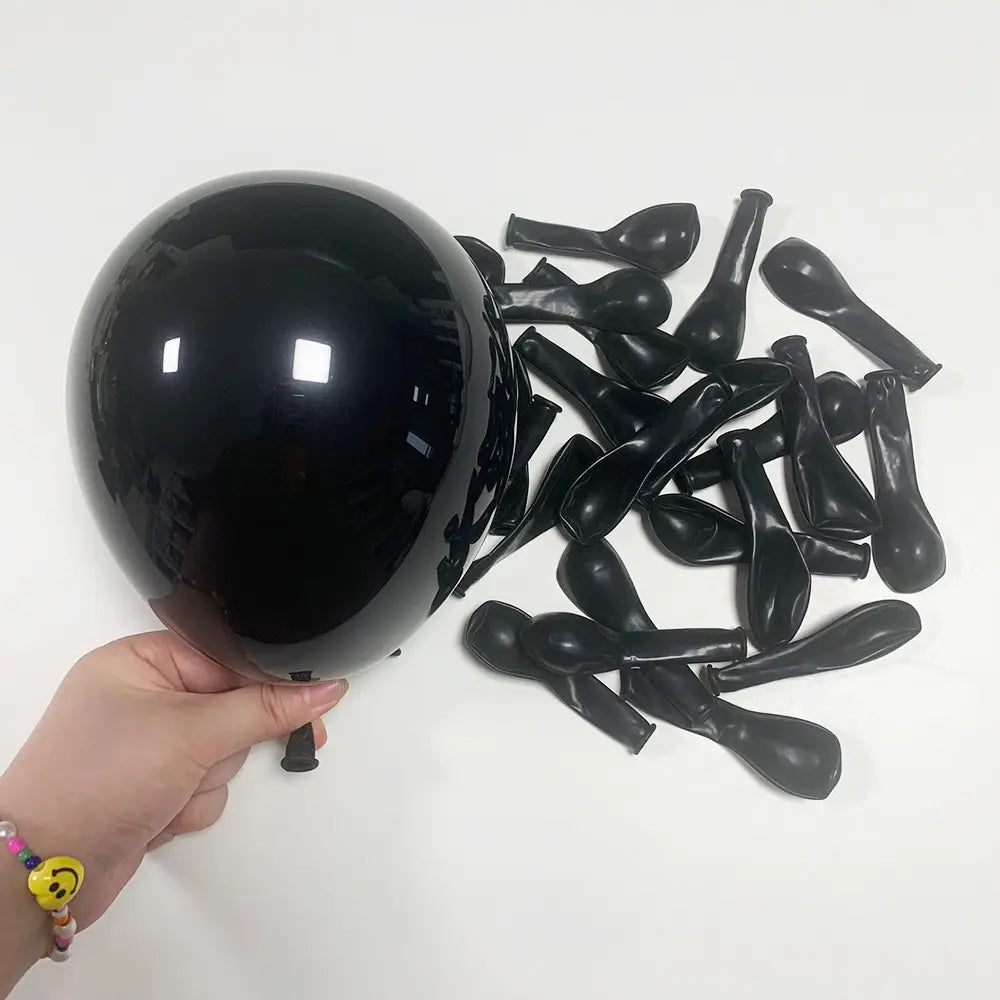 Ein glänzender schwarzer Latexluftballon, der in einer Hand gehalten wird, mit mehreren nicht aufgeblasenen schwarzen Ballons in der Nähe, aus dem roten schwarzen weißen Ballon-Set für die Partydekoration.
