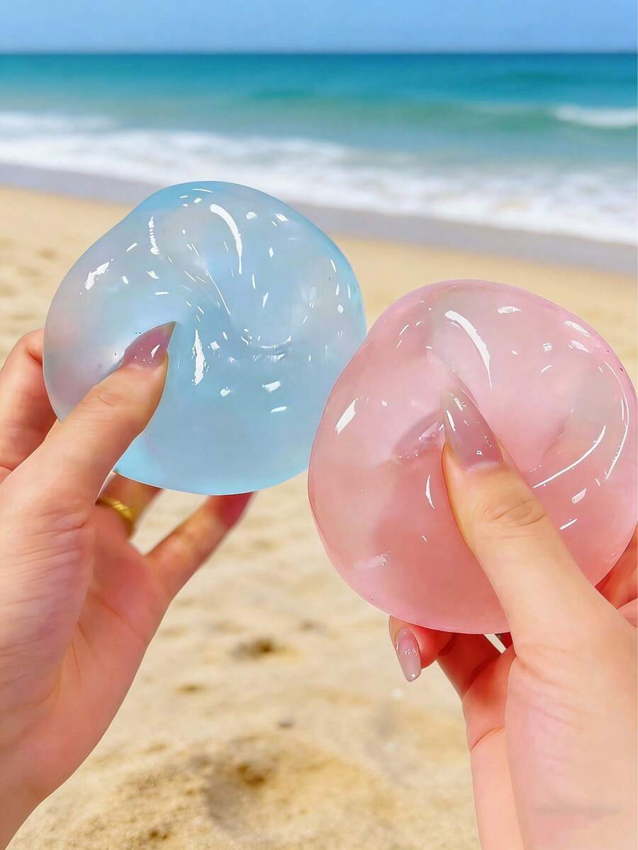Deux balles compressibles translucides ressemblant à un gel pour soulager le stress, tenues dans les mains, d’un bleu clair et d’un rose, sur un arrière-plan de plage, avec la mention « Blue Coconut Oil »