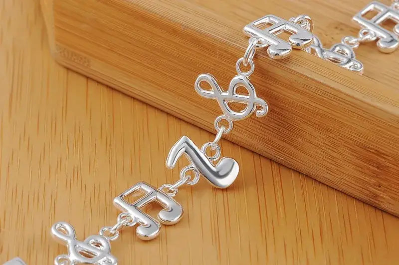 Silver musical note sterling silver bracelet featuring a polished reflective finish with alternating treble clef and eighth note charms.