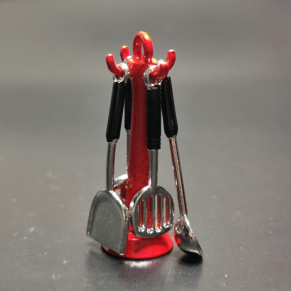 Ensemble d’ustensiles de cuisine miniature pour maison de poupée comprenant un support en plastique rouge tenant des petites cuillères, spatules et louches en métal argenté, avec des poignées noires.