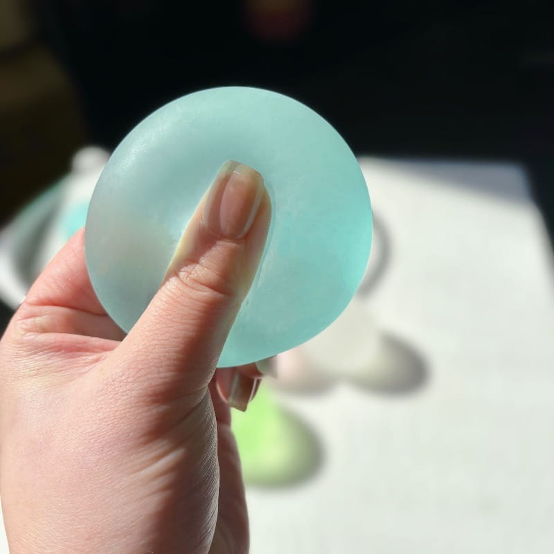 A translucent light blue mochi squeeze sensory fidget toy made of squishy material being held in a hand.