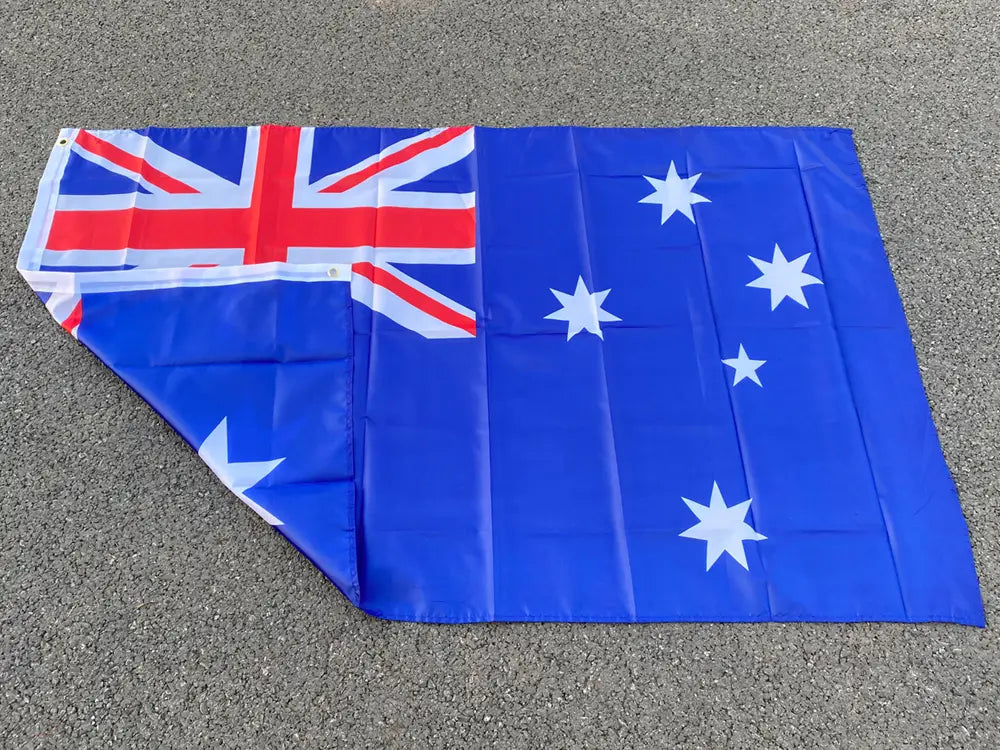 Bandera nacional australiana azul de 90x150 cm que muestra un aspa de la bandera británica roja y blanca en la esquina y cinco estrellas blancas sobre un campo azul intenso, vista de frente.