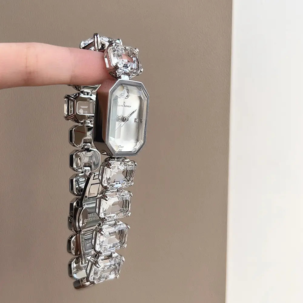 A sparkling silver women’s quartz watch with an octagonal face and a bracelet adorned with large clear emerald-cut crystals featured in a rose gold rectangular design.
