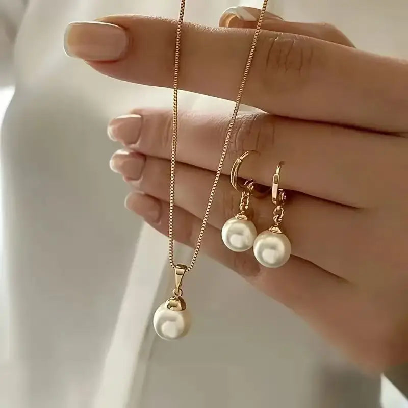 Un ensemble délicat de bijoux en perles dorées rosées, comprenant un collier à pendentif et des boucles d’oreilles créoles assorties, avec une seule perle de culture blanche de rivière suspendue à de fines chaînes.