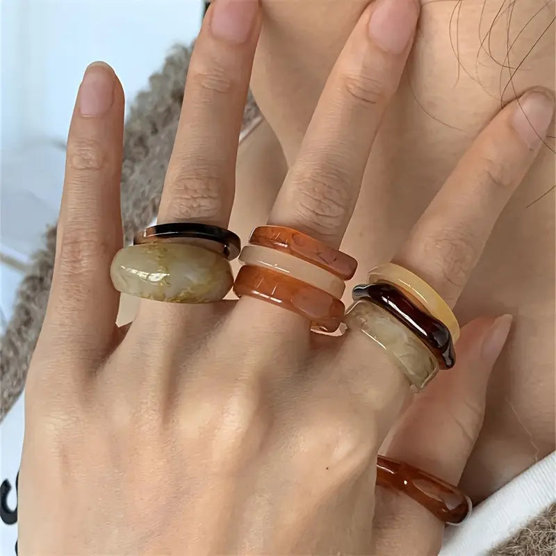 A hand displaying a bohemian retro style resin stackable ring set featuring wide, stacked rings in earthy amber, brown, and cream tones made from resin material.