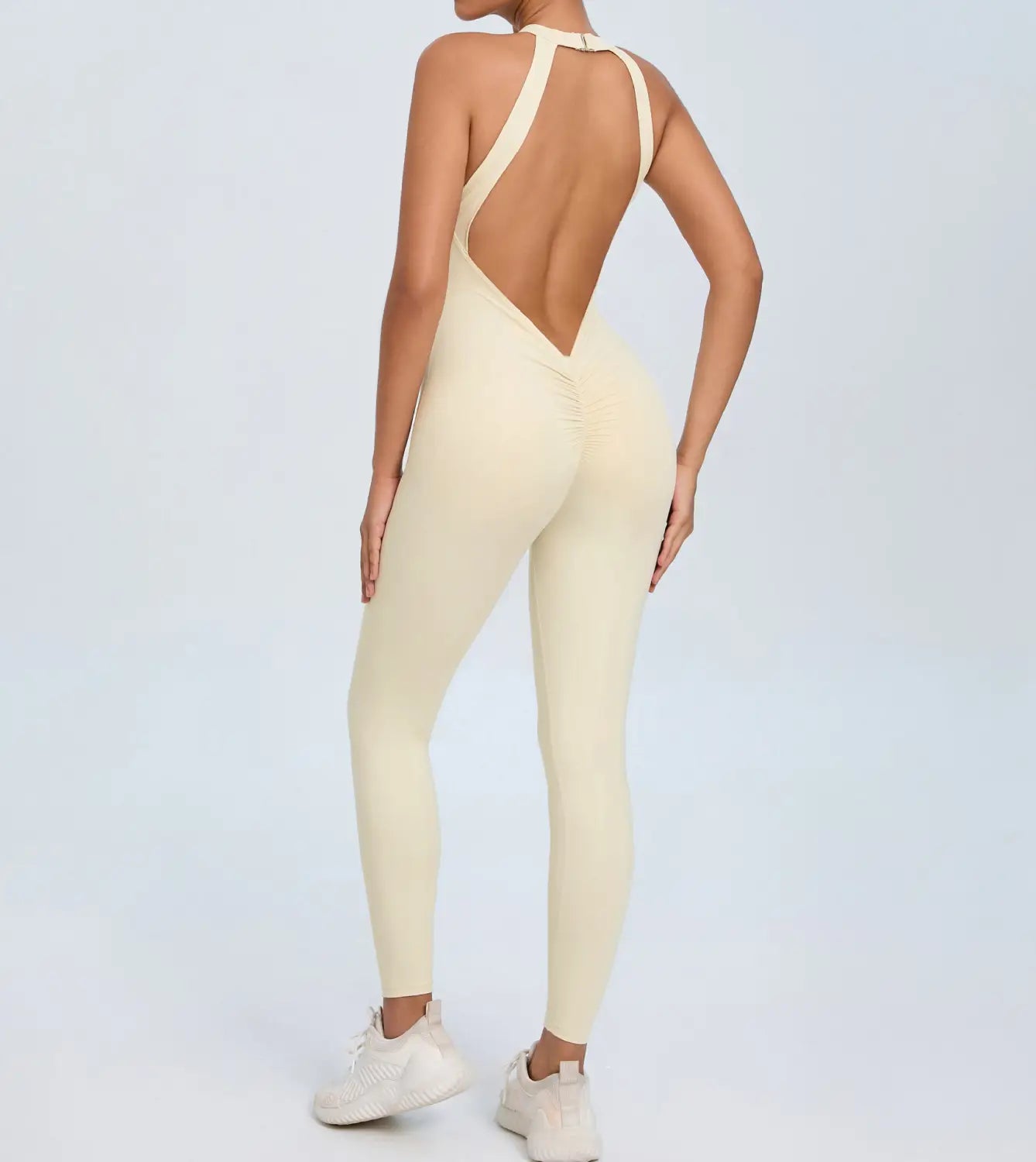 Cream-colored form-fitting one-piece athletic bodysuit with a backless design and ruched detailing shown from the back side.