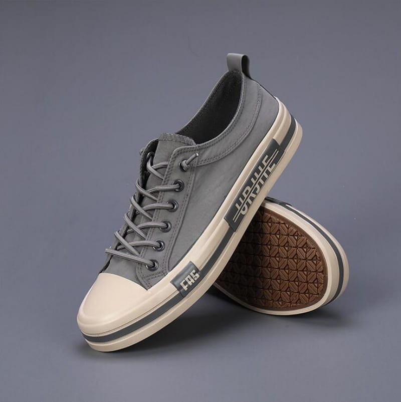 Baskets décontractées en toile pour hommes, chaussures d’été légères en gris, avec une coque en caoutchouc blanc et des rayures contrastées noires sur le côté, avec des lacets gris assortis.