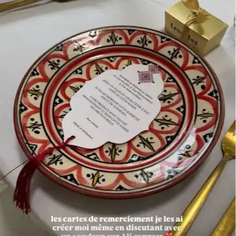 assiette décorative en céramique à motif rouge et noir avec un pompon ornemental fixé en son centre, présentée comme une faveur personnalisée de carte cadeau de parfum de mariage
