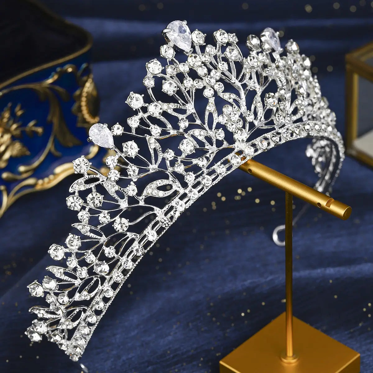 Une tiare de mariage en cristal d'argent étincelant, présentant des motifs de feuilles délicats, de nombreux cristaux transparents, et deux pierres plus grandes en forme de poire en partie supérieure.