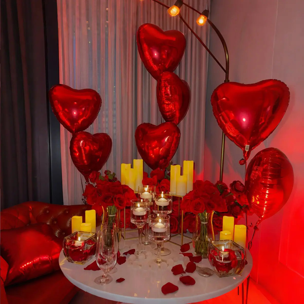 Red metallic heart-shaped balloons featured in an anniversary decoration set with rose petals.