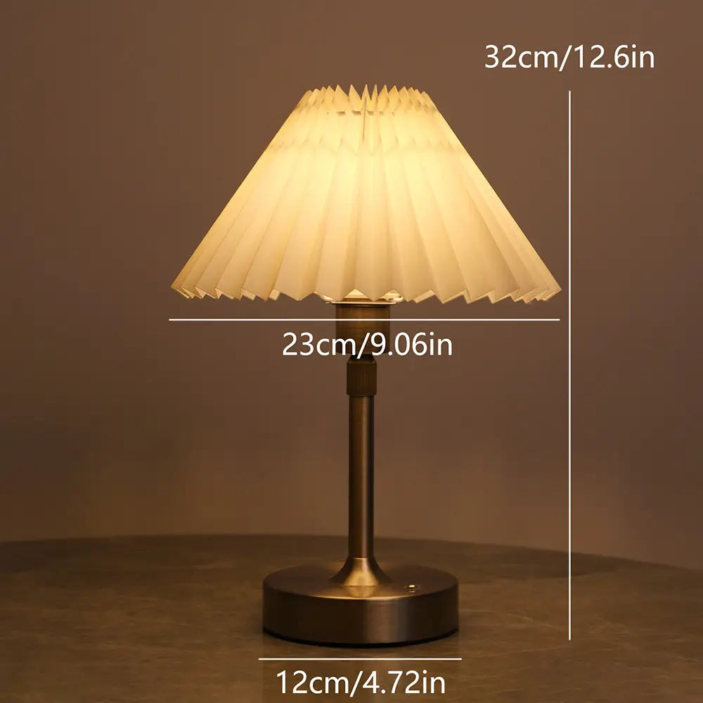 Ein warmtoniger, plissierter Papierschirm mit messingveredelter Metallbasis und -stange in einer plissierten Messing-Touch-Tischlampe.