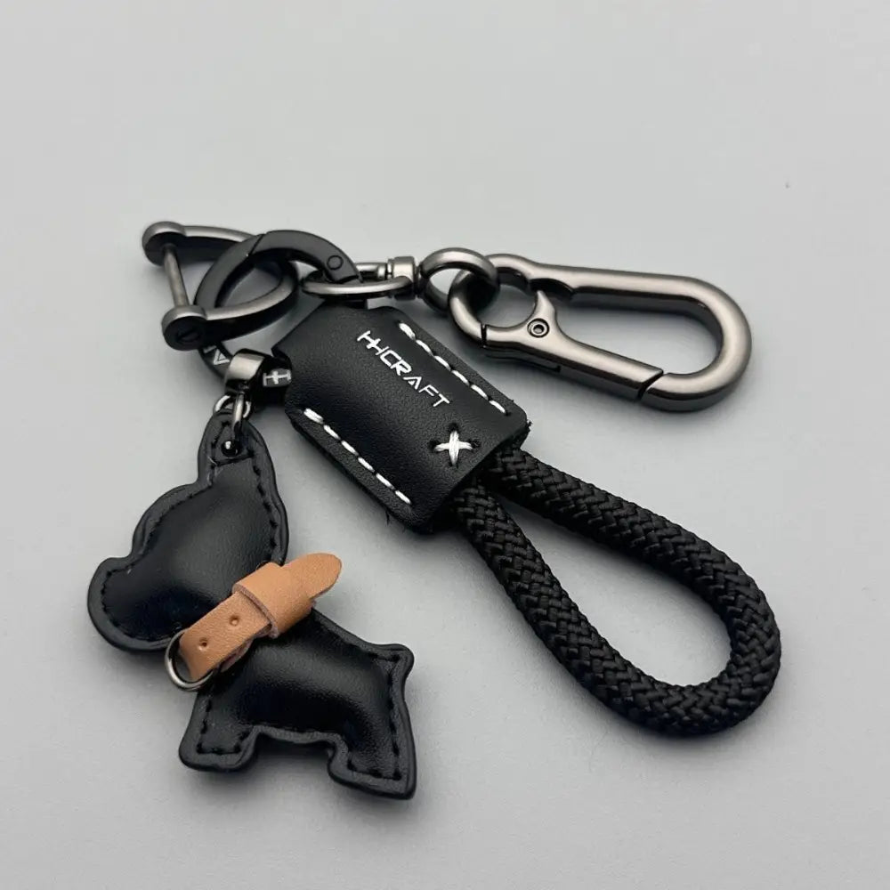 Black leather French Bulldog keychain with braided black cord silver-toned carabiner clips and small dog-shaped charm with tan leather accents.