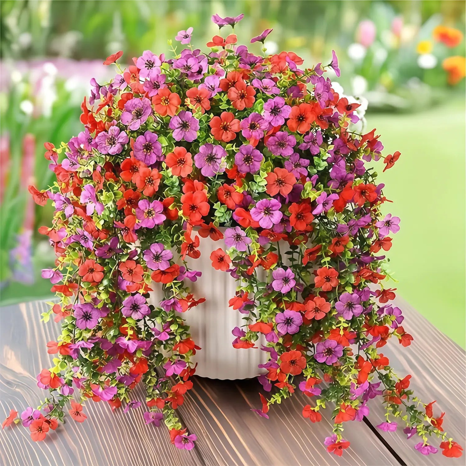 A vibrant cascading artificial flower bouquet featuring morning glory vines and eucalyptus with red and purple blooms in a white ceramic pot.