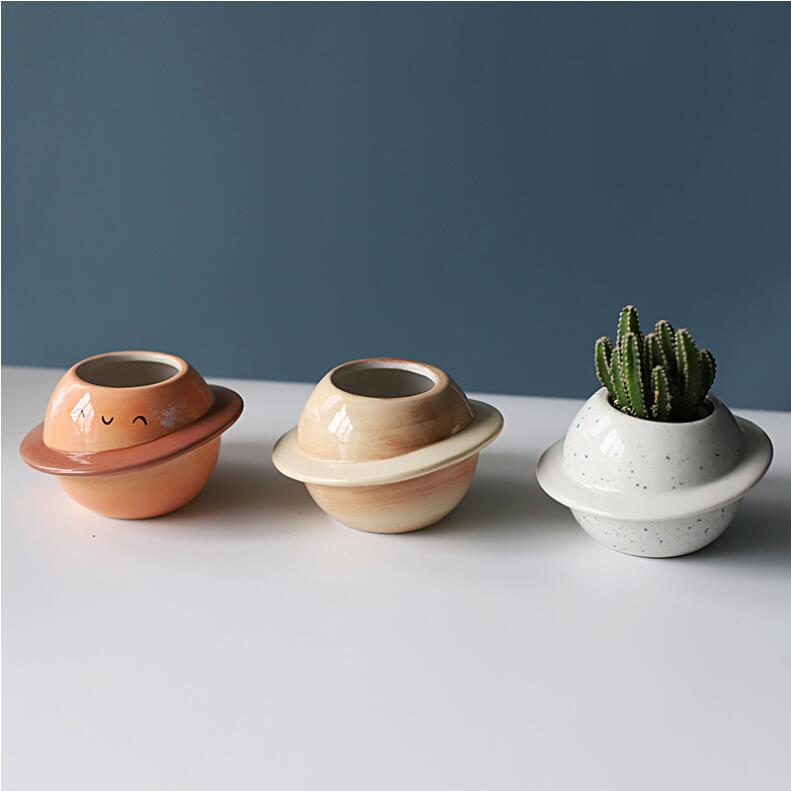 Drei Keramik-Sukkulenten-Töpfe in Planetform in Terrakotta-Orange mit lächelndem Gesicht, Beige mit glatter Oberfläche und weiß gesprenkelt, die einen grünen Kaktus aufnehmen.