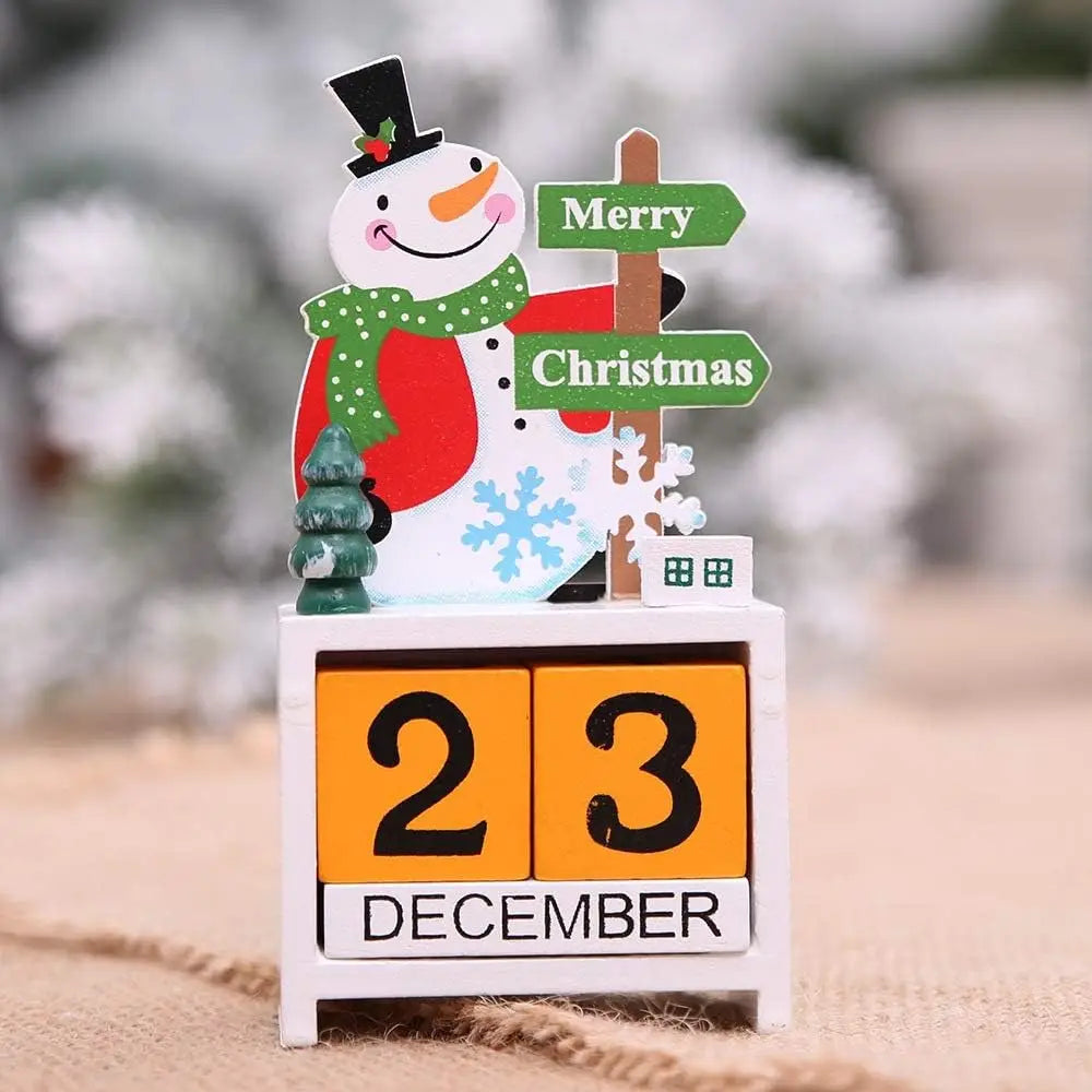 A cheerful wooden Christmas countdown calendar block features a snowman figurine with a black top hat, green polka-dot scarf, and red coat standing atop white calendar blocks displaying 23 December on orange panels.