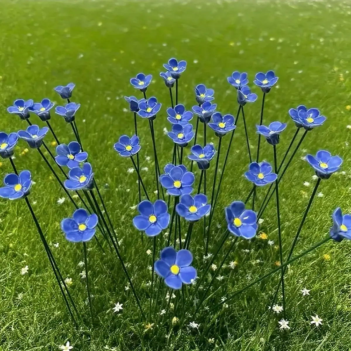 blue ceramic artificial flowers resembling forget me nots with yellow centers arranged on slender black stems for decorating vases
