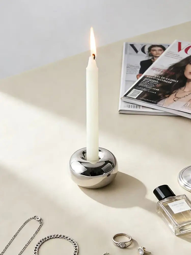 A sleek silver ceramic sphere candle holder with a polished metallic finish holds a tall white taper candle.