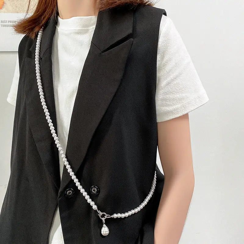 Un long collier délicat en perles à l’aspect argenté, en pendentif pour femmes, avec un pendentif en forme de goutte porté en bandoulière au-dessus d’un gilet noir.
