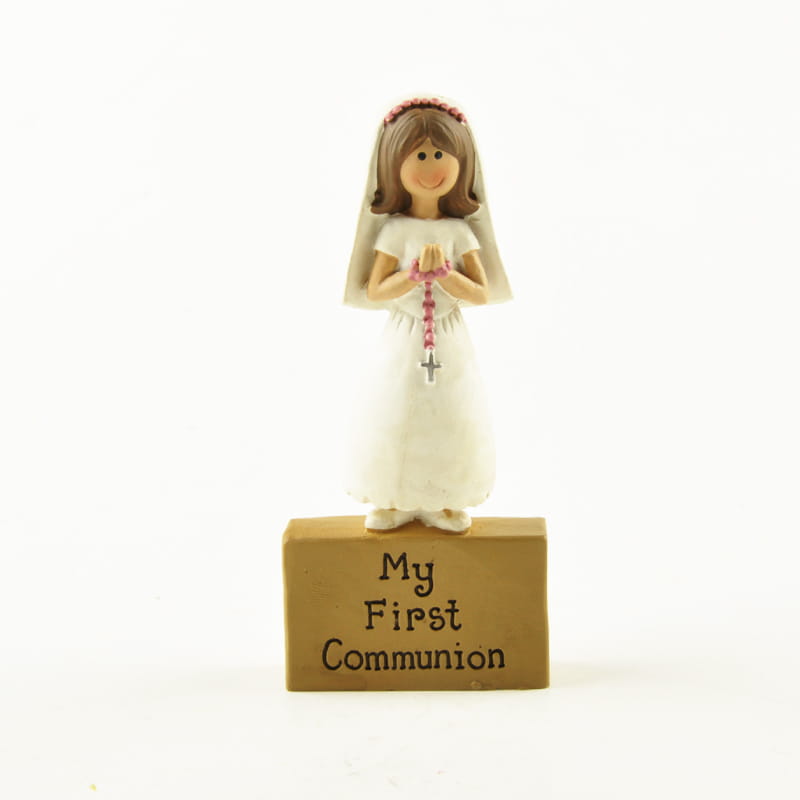 une figurine en résine blanche d’une jeune fille souriante en tenue de communion, aux cheveux bruns et portant un voile, tenant un chapelet rose pour la décoration de table de première communion
