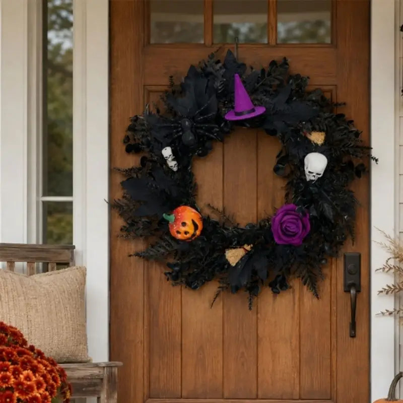 Halloween-Kranz mit schwarzem Grund, verziert mit einem violetten Hexenhut, weißen Totenköpfen, einer orangefarbenen Kürbiskugel und einer violetten Rose zur saisonalen Dekoration.