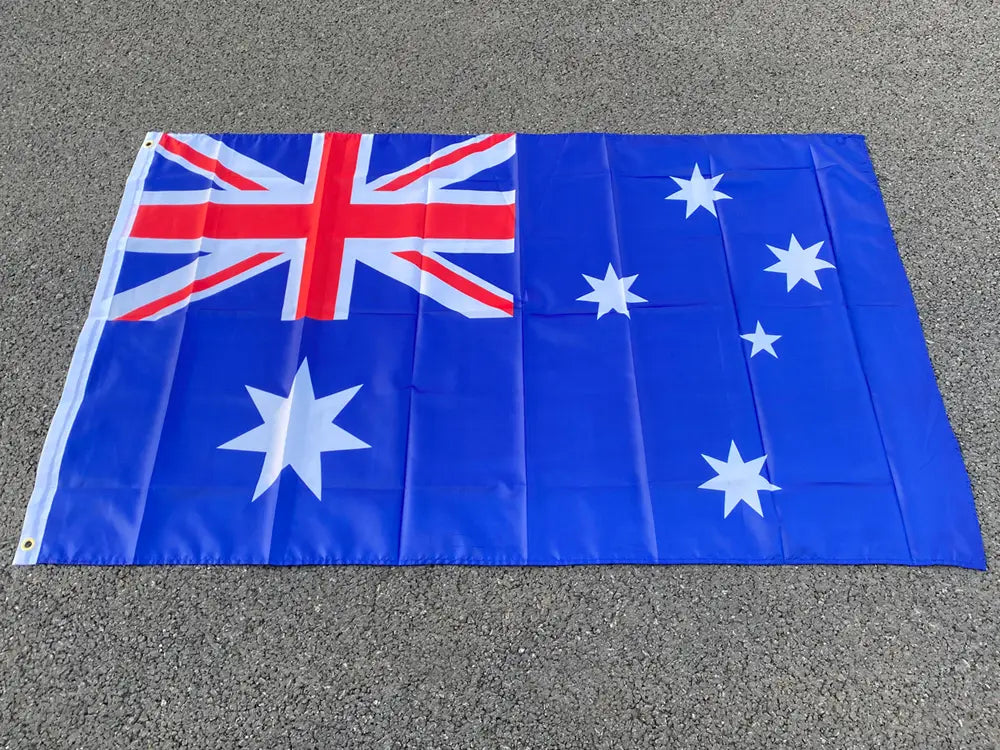 Bandera nacional australiana azul de 90x150 cm con un aspa de la bandera británica roja y blanca en la esquina, que presenta una gran estrella de siete puntas y cinco estrellas más pequeñas sobre un campo azul, vista de frente.