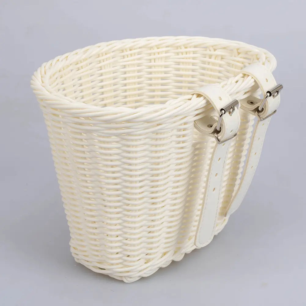 Cream-colored woven kids bicycle basket with white leather straps and silver metal buckles from the kids woven bicycle basket set with bell and tassels.