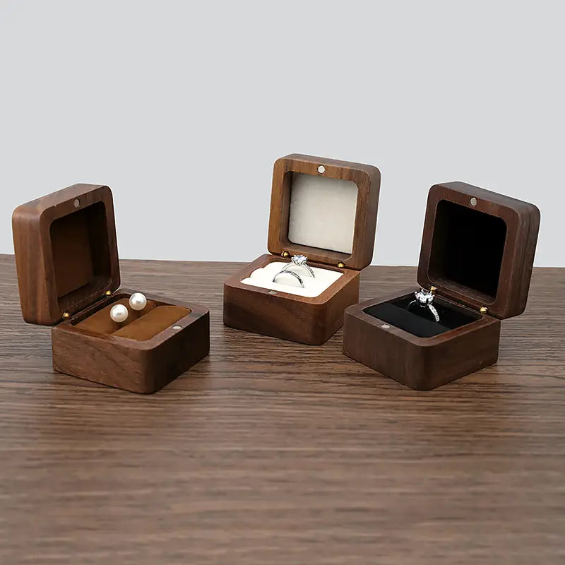 Trois présentoirs en bois brun foncé pour bague d’engagement et proposition de mariage, ouverts pour présenter différents bijoux d’exception.