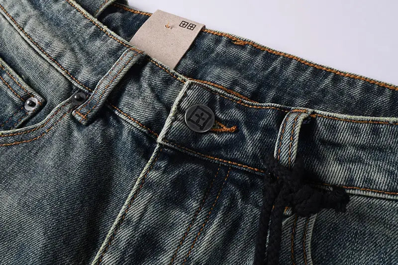 Men’s distressed blue acid wash denim shorts with dark-wash denim fabric, a black button featuring a white logo, and contrasting orange stitching.