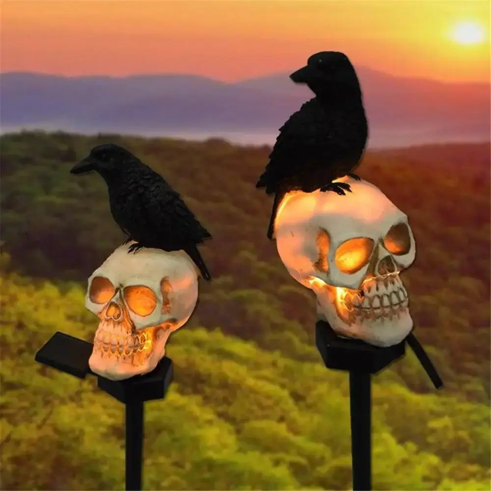 lampes solaires de jardin en forme de crâne blanc, avec des intérieurs orange lumineux, surmontées de figurines de corbeaux noirs, pour la décoration d’Halloween