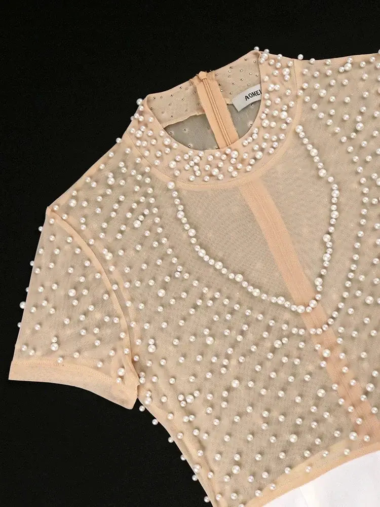 Beige sheer top with scattered white pearls and a delicate pearl necklace detail complementing the beaded high waisted jumpsuit elegant party outfit.