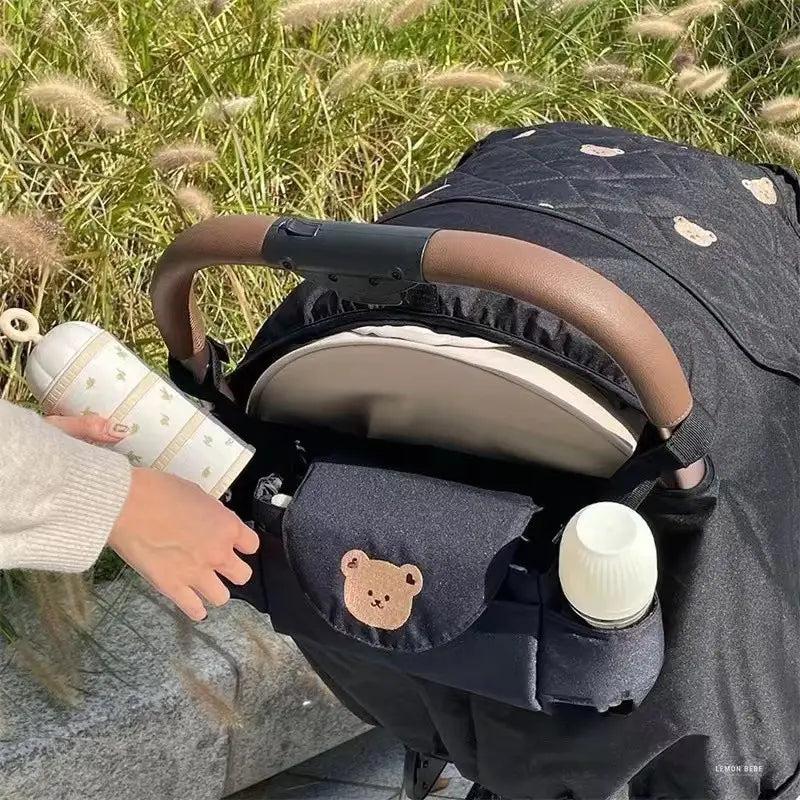 刺繍のクマの顔が施されたキルティングのブラックのベビーカー用オーガナイザーバッグ。収納に便利な、揃いの取っ手グリップ付き。