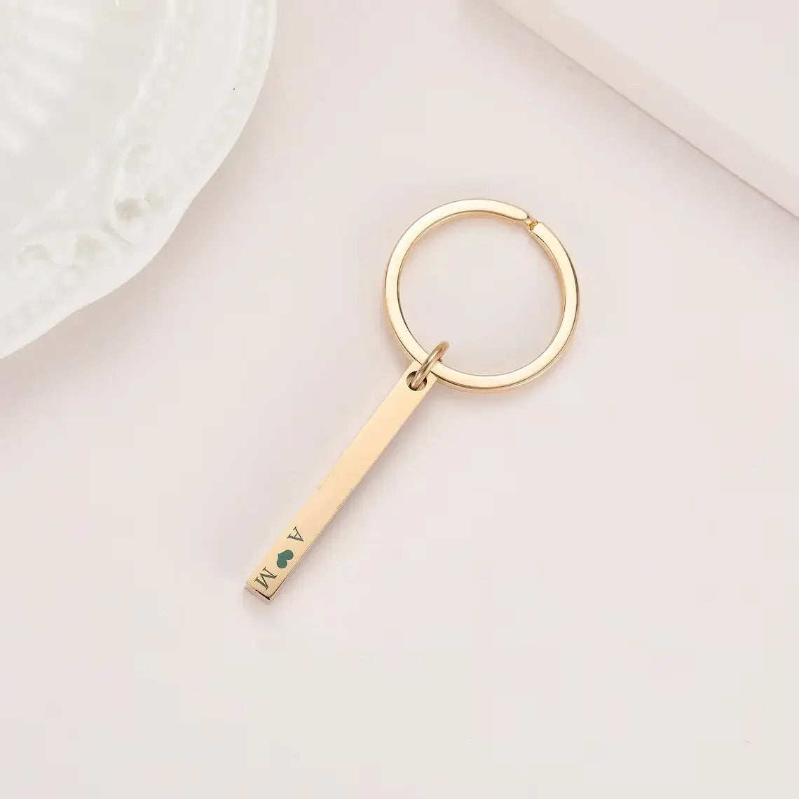 Gold-colored stainless steel custom engraved 4d bar keychain with a circular ring featuring engraved initials a and m separated by a small green heart.