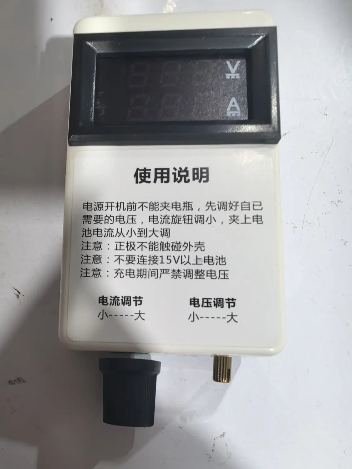 Chargeur de batterie en plastique blanc pour régulateur de courant et de tension numérique avec écran numérique noir affichant les mesures de tension et de courant et deux boutons de réglage, avec indications pour l’intensité et les volts.