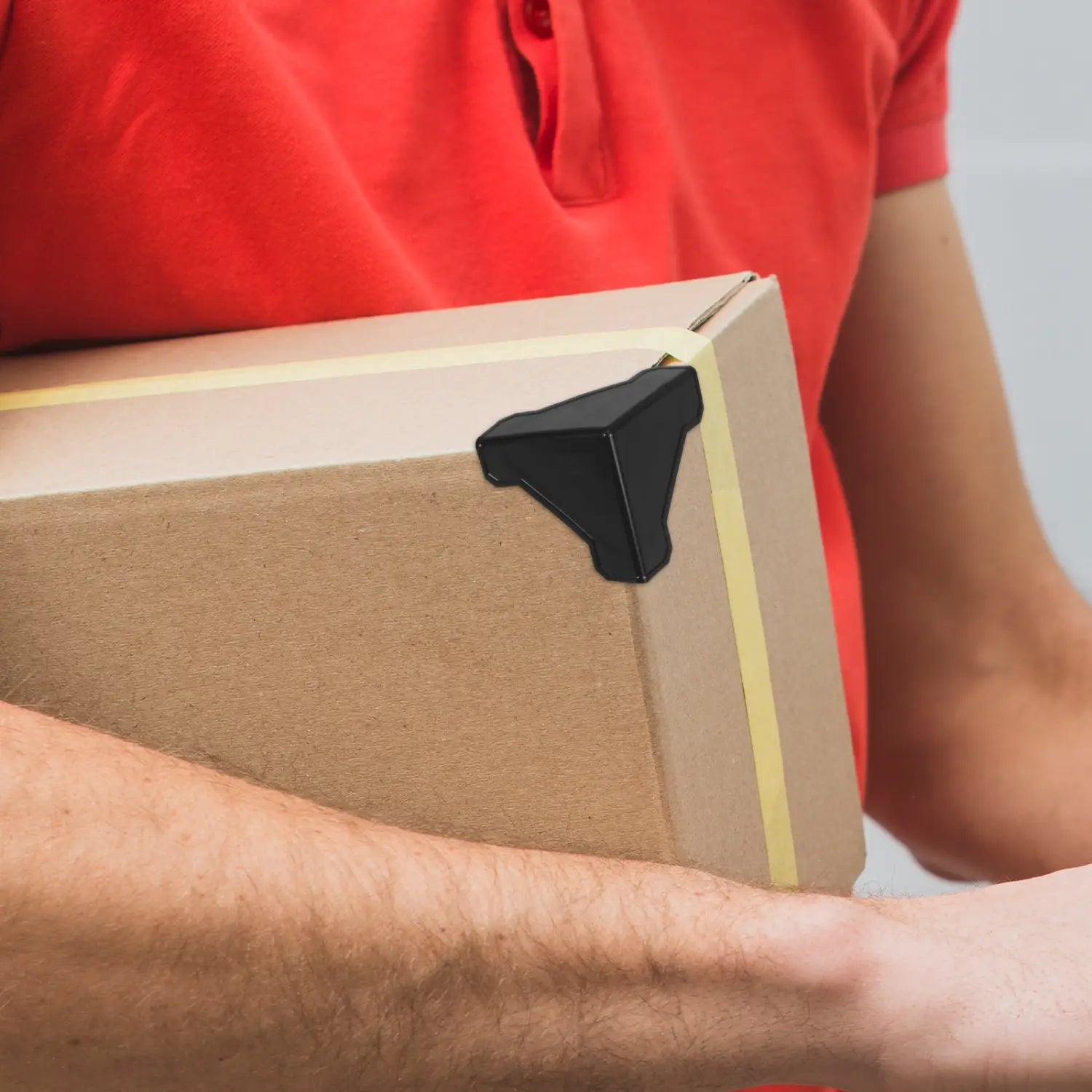 Schwarzer dreieckiger Eckschutzwinkel aus strapazierfähigem Material auf einer braunen Pappkartonverpackung, verwendet als Verpackungsecke für Kartonverpackungen in einem Set von 100 Stück Eckschutzwinkeln.