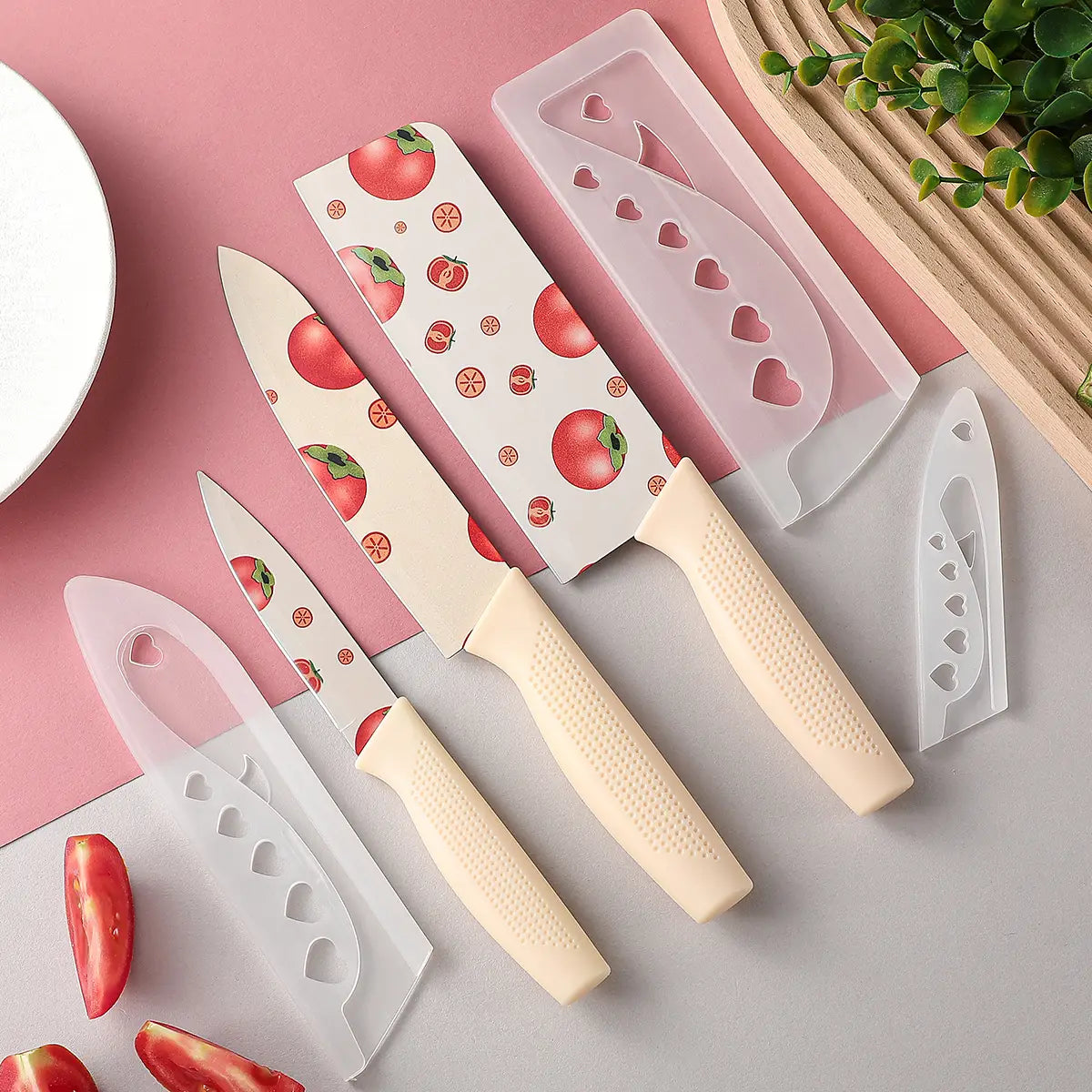 Set of four ceramic kitchen knives with tomato-patterned blades and cream-colored textured handles with matching heart-patterned protective sheaths.