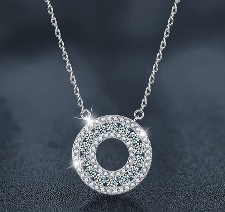 Collar con colgante de halo de moissanita de plata con brillo, con un colgante circular adornado con varias filas de cristales facetados transparentes engastados en un marco metálico elegante.
