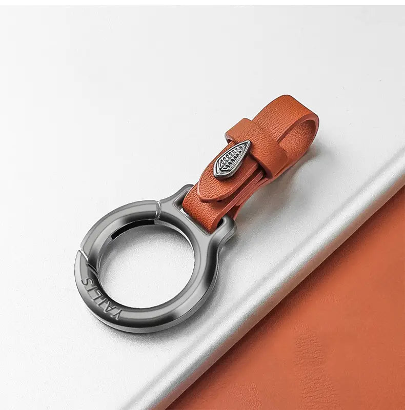 Beiger Lederschlüsselanhänger für den Pkw, mehrzweckiger Anti-Verlust-Halter, mit silberner Metallklemme und eingraviertem Logo.
