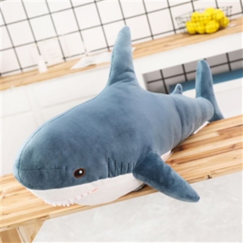 A plush blue shark stuffed animal pillow with a white underbelly and stitched details made of soft fabric material.
