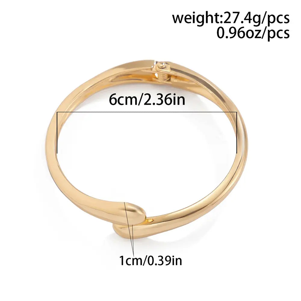 Wide metal bangle in gold tone with a sleek, smooth curved design and a secure clasp as a chunky open cuff bracelet.