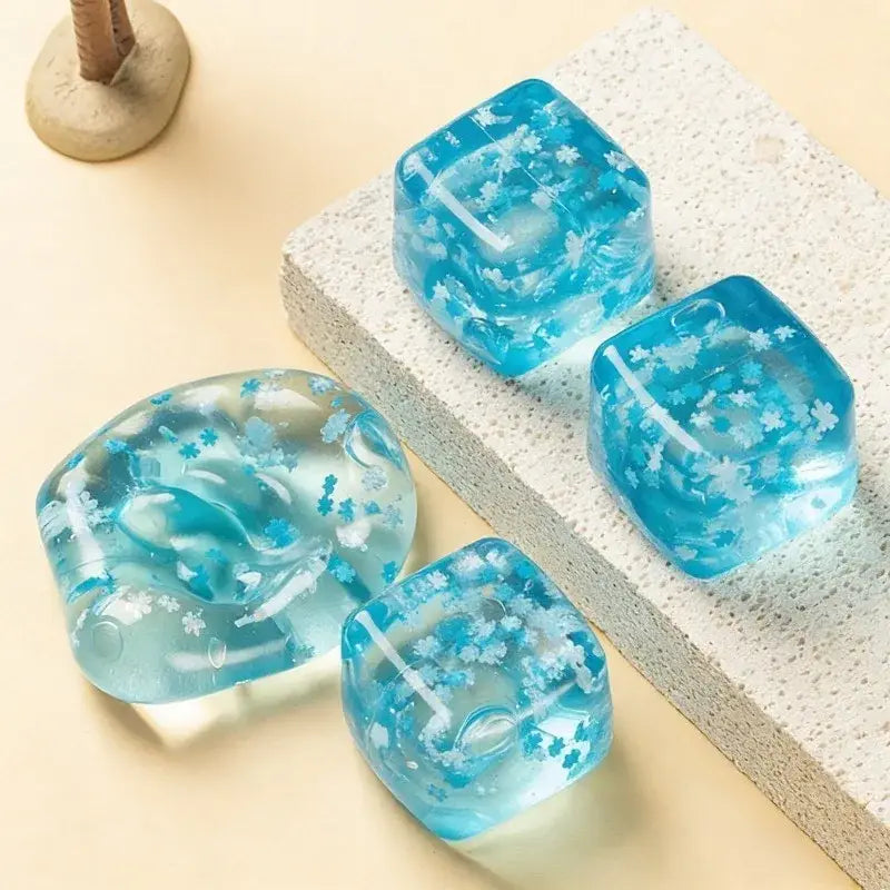 ein klarer blauer Eiswürfel mit Schneeflocken-Motiv zur Stressreduktion aus Harz, mit eingebetteten weißen floralen Mustern in einer Vorderansicht.