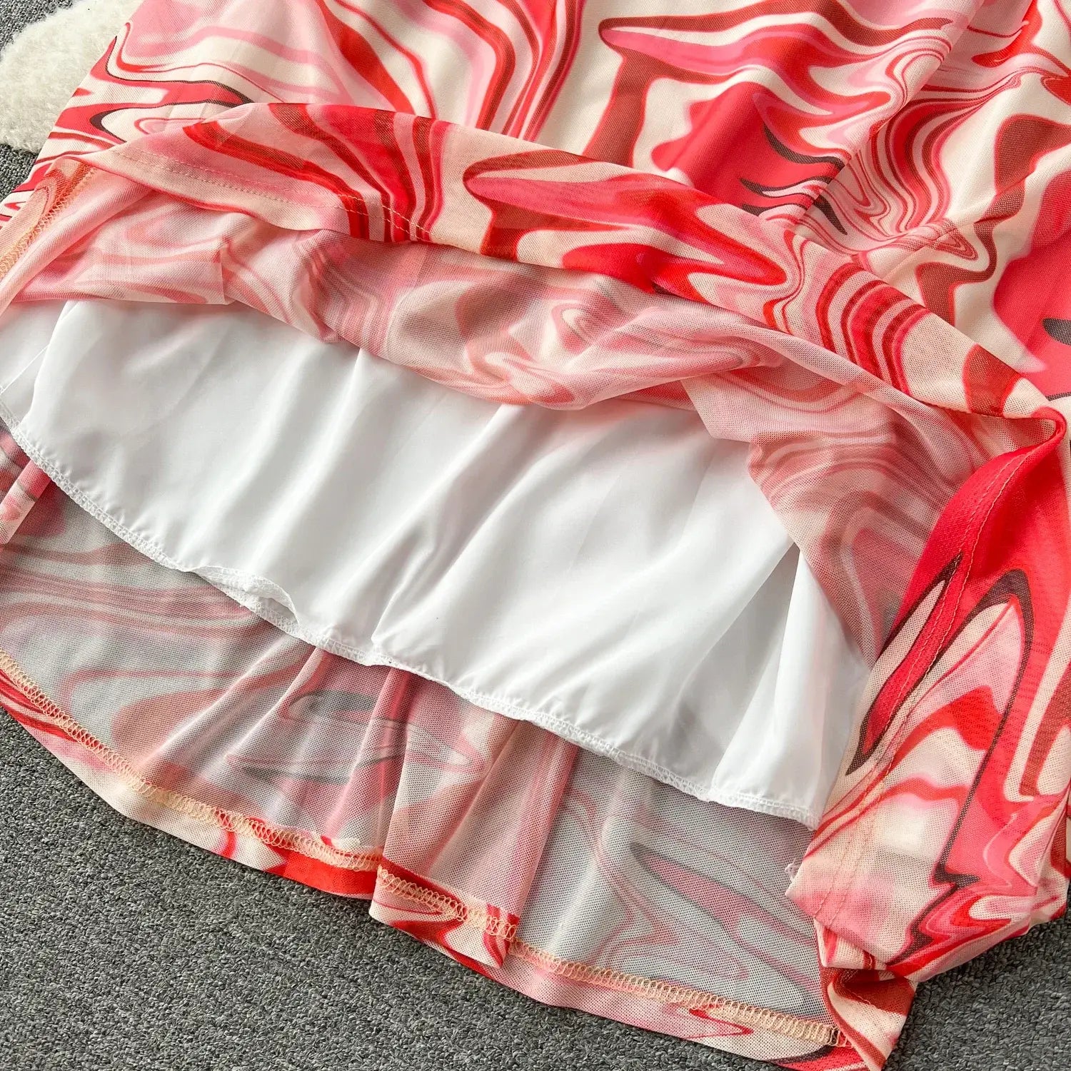 a two piece mesh skirt set featuring a flowing sheer dress with a vibrant red and pink marbled pattern over a solid white lining and an elastic closure type