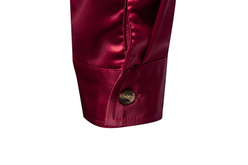 Manschette aus tiefrotem Satin mit Metallknopf an einem Herrenhemd mit goldfarbenem Besatz aus Satin.
