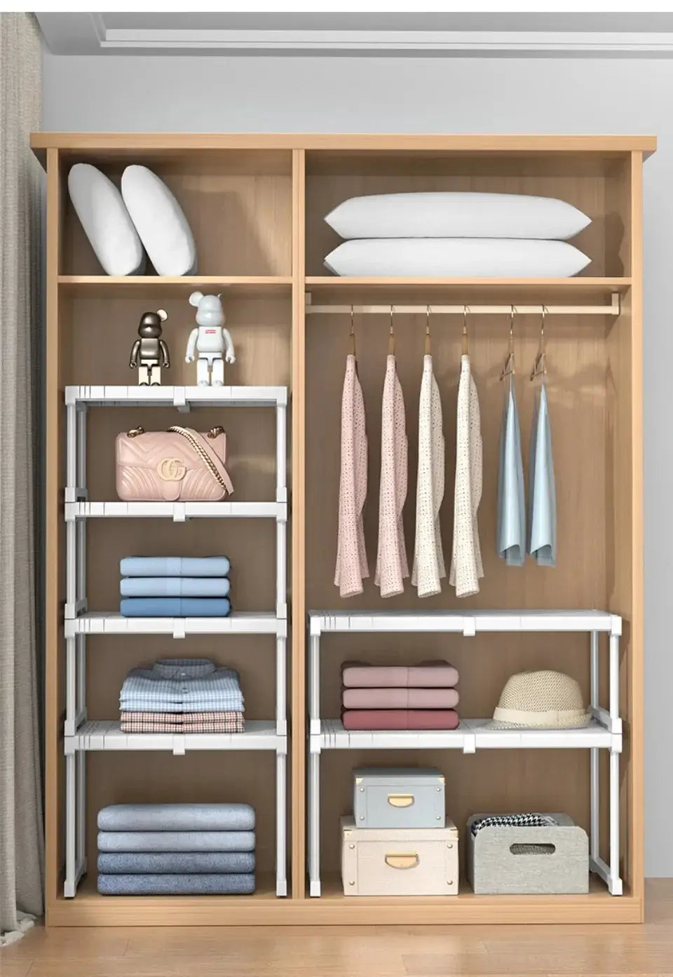 Organisateur d’armoire à cadre en bois clair avec étagères métalliques empilables blanches réglables et barres de suspension tenant des vêtements pliés avec des coussins, un sac à main rose et des boîtes de rangement.