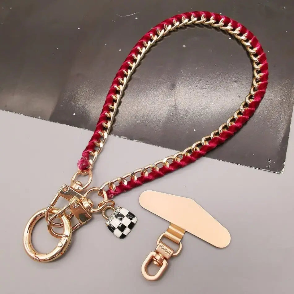 Handy-Handgelenkriemen aus goldfarbener Kette mit rotem geflochtenem Kord, goldfarbenen Metallverbindern und einem schwarz-weiß karierten Schloss-Anhänger, entworfen für Anti-Lost-Handylanyard-Verwendung.