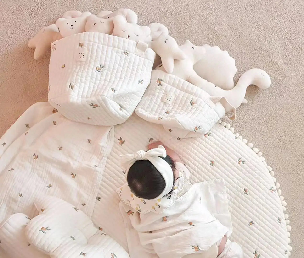 Ein weiches, weißes, gepolstertes Babywindel-Aufbewahrungskörbchen mit subtiler Blattmusterung, sanft gerafften Kanten und gemütlicher Haptik.